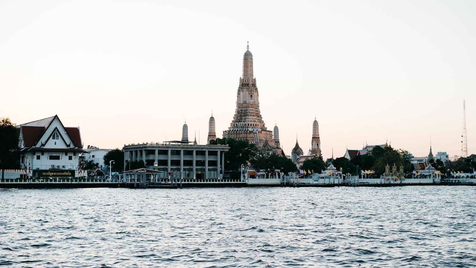 Wat Arun temple glowing at dusk on the Chao Phraya river in Bangkok, Thailand